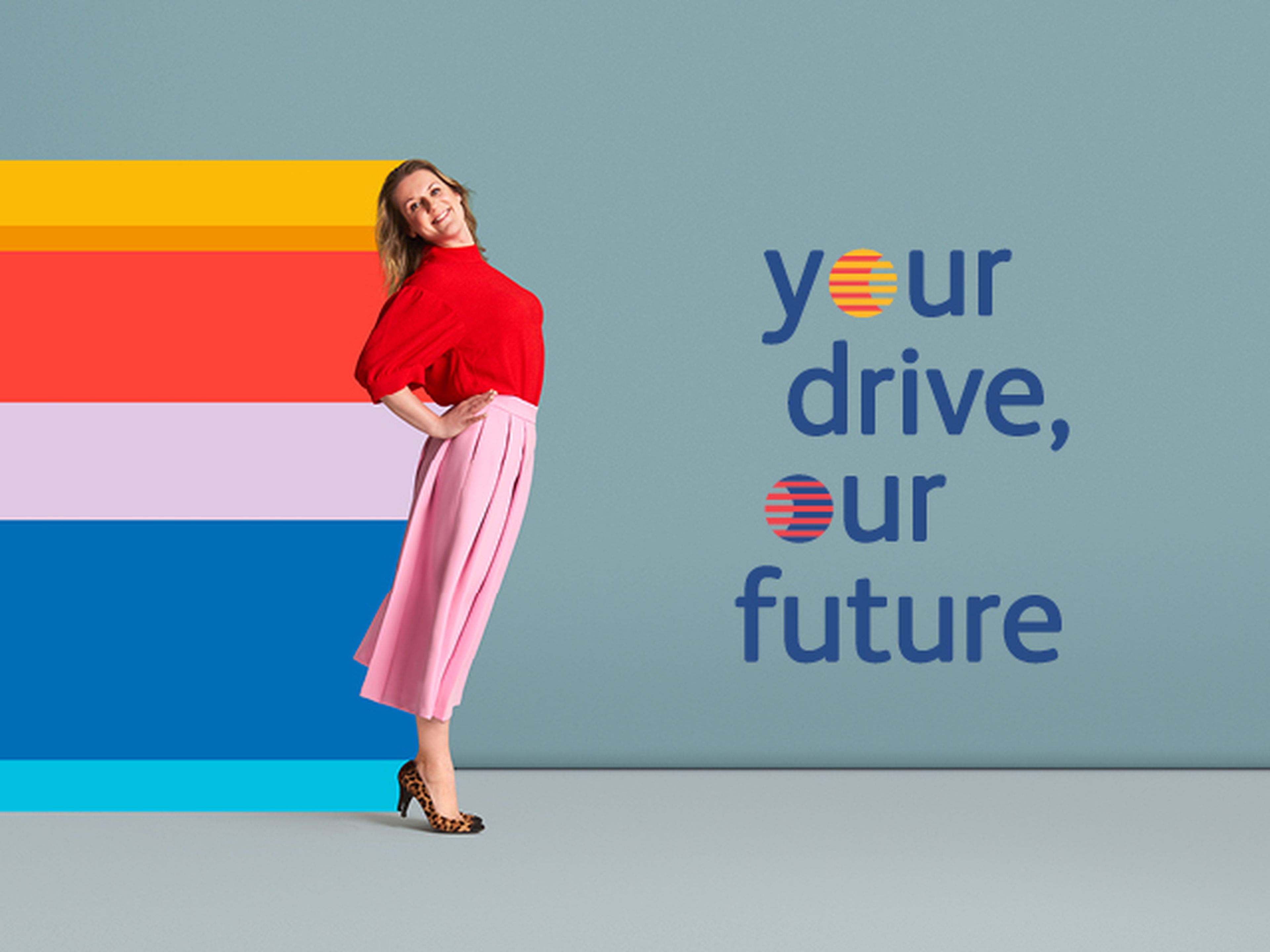Een vrouw poseert vrolijk met een lichte buiging naar achteren tegen een effen blauwe achtergrond. Ze draagt een rode top, een roze geplooide rok tot halverwege de kuit en luipaardprint-hakken.