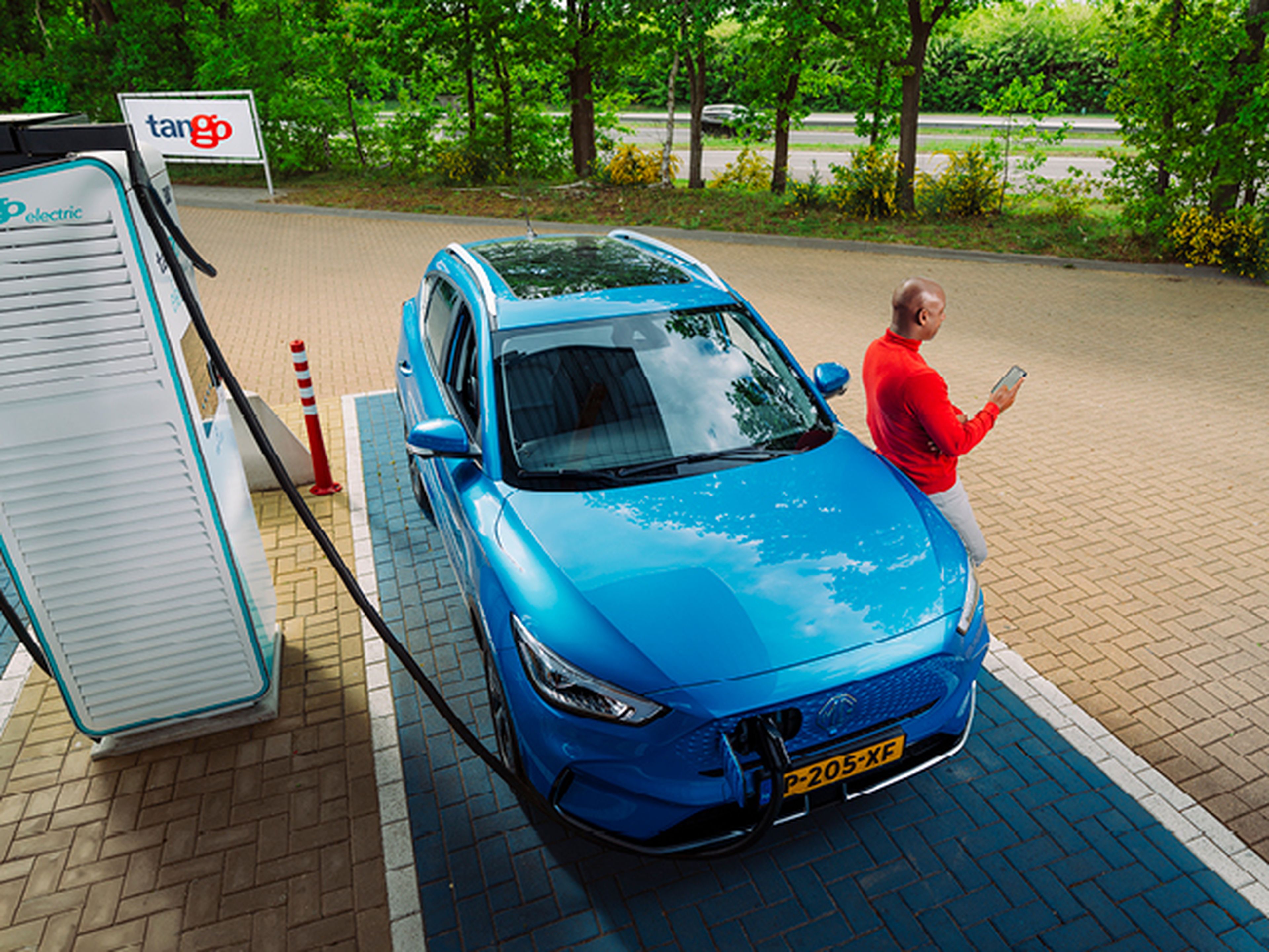Man leunt tegen blauwe MG tijdens het laden van zijn auto bij Tango electric