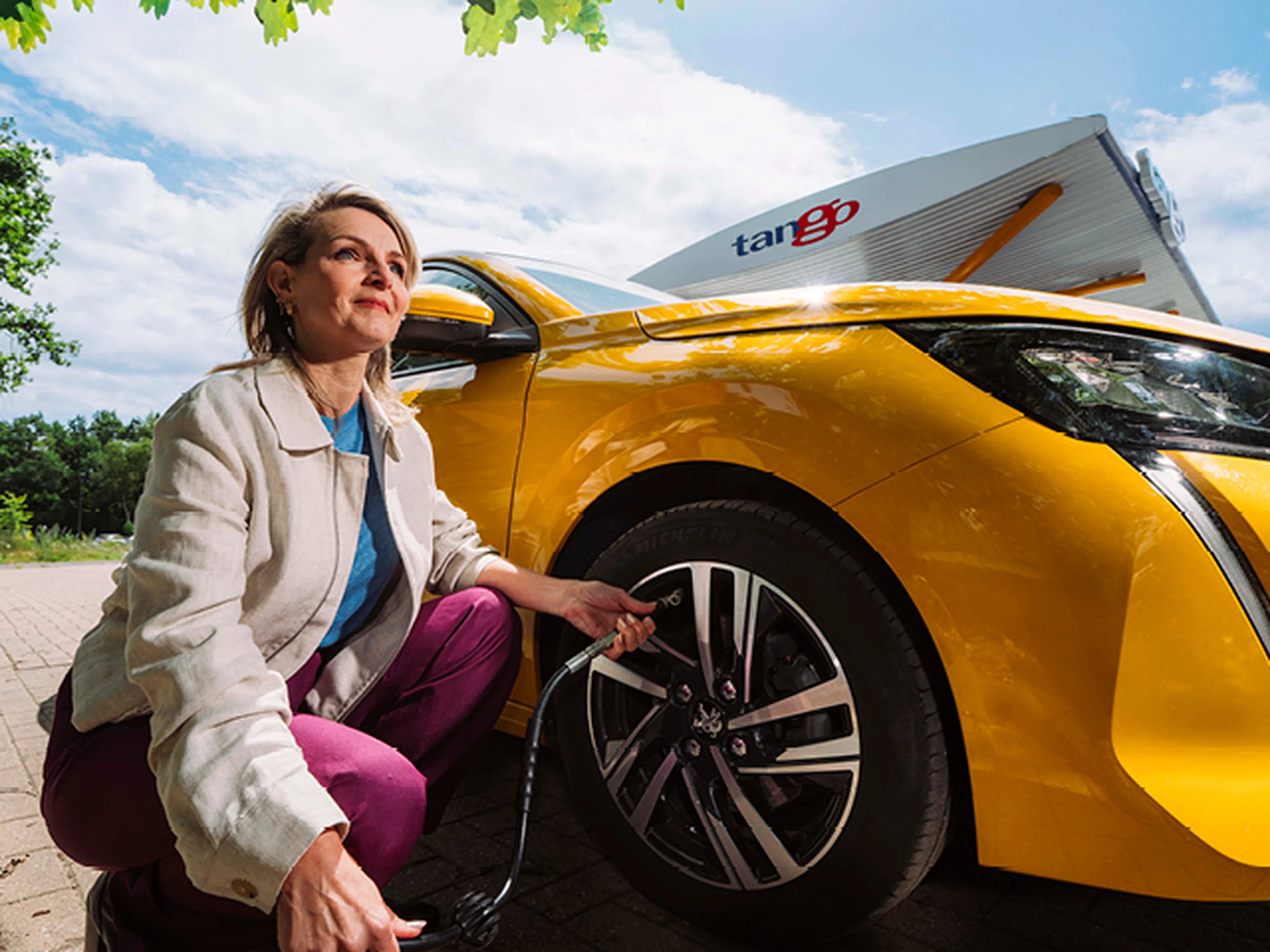 Vrouw die bij Tango banden oppompt van gele peugeot 208