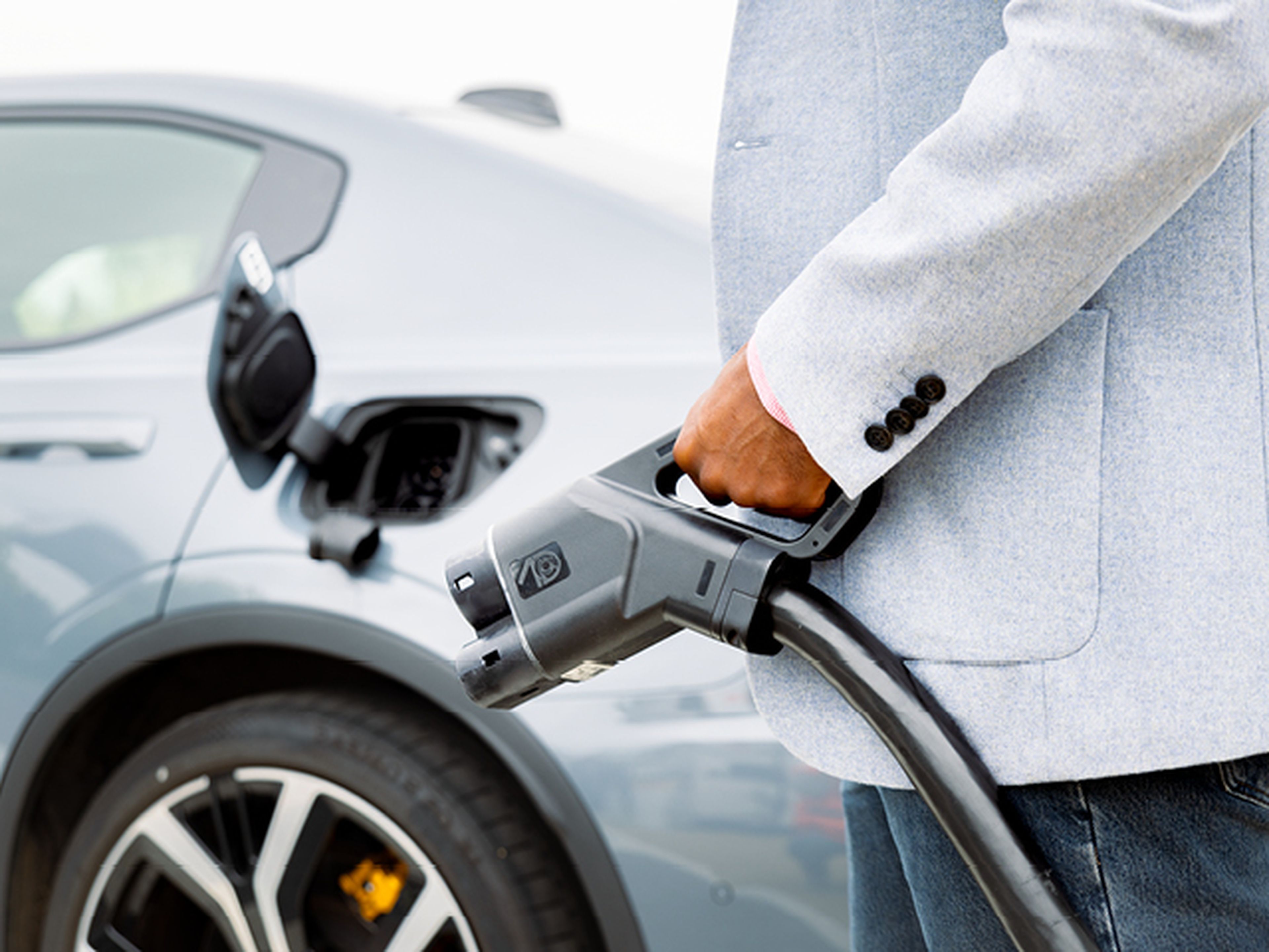Man in grijze pas houdt laadkabel vast naar grijze polestar 2