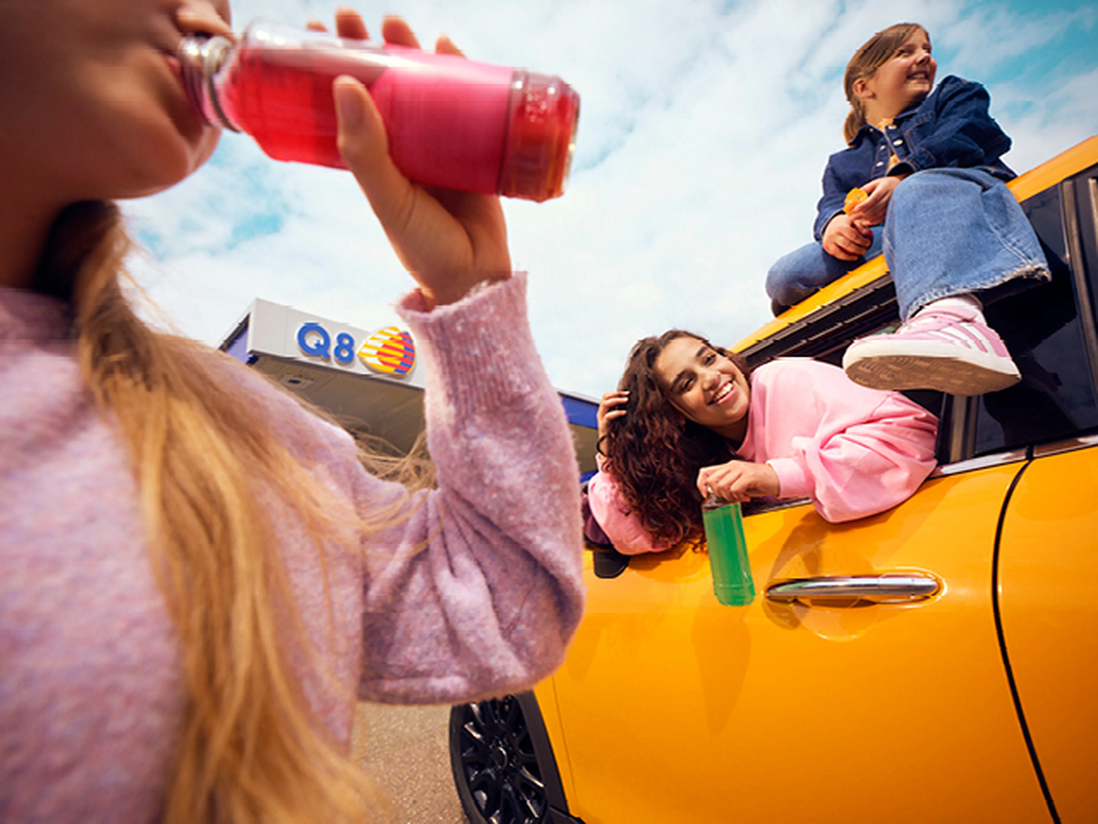 Kinderen eten en drinken aan Q8 station naast gele mini