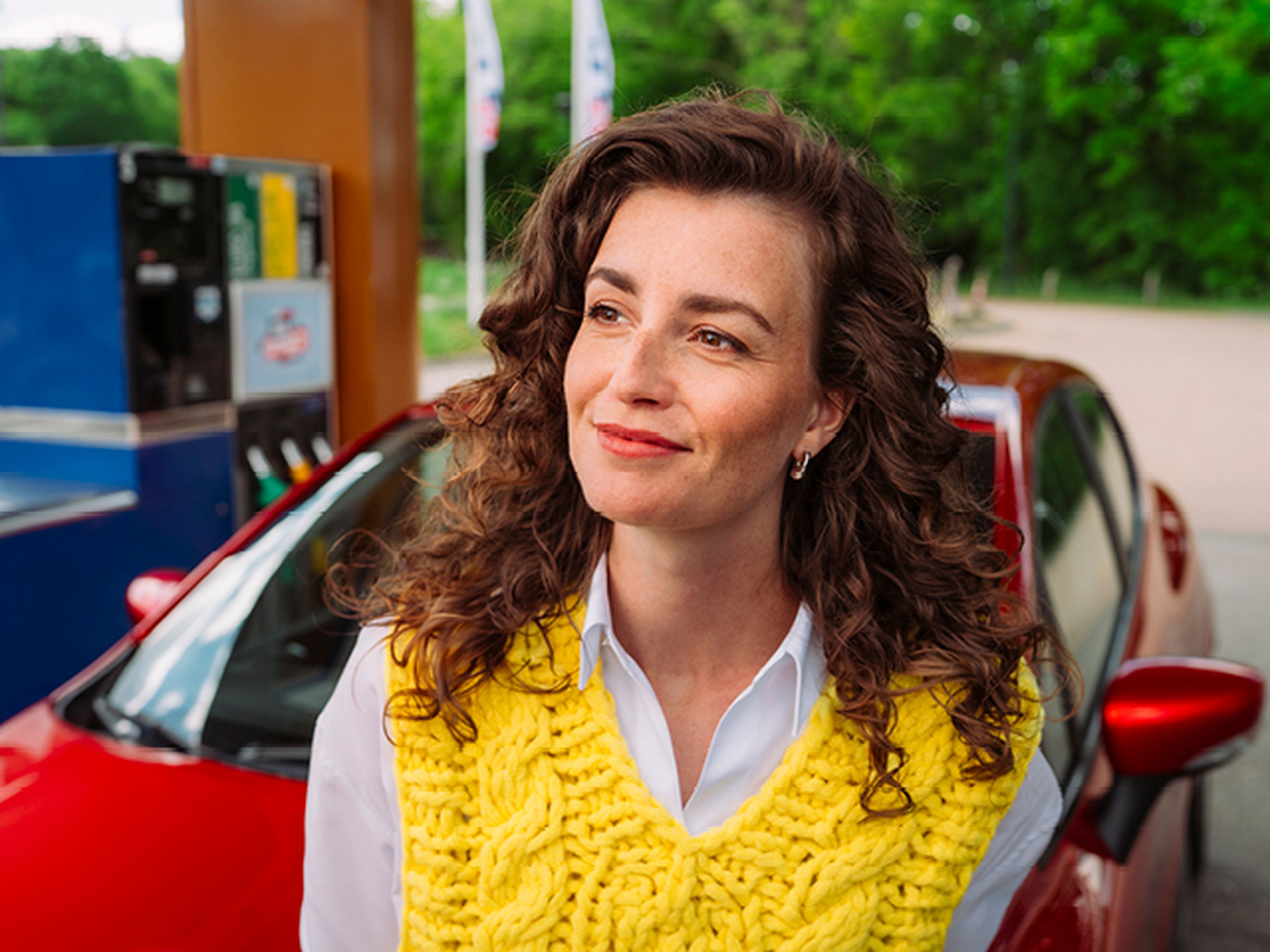 Vrouw staat glimlachend bij een Tango tankstation naast haar auto