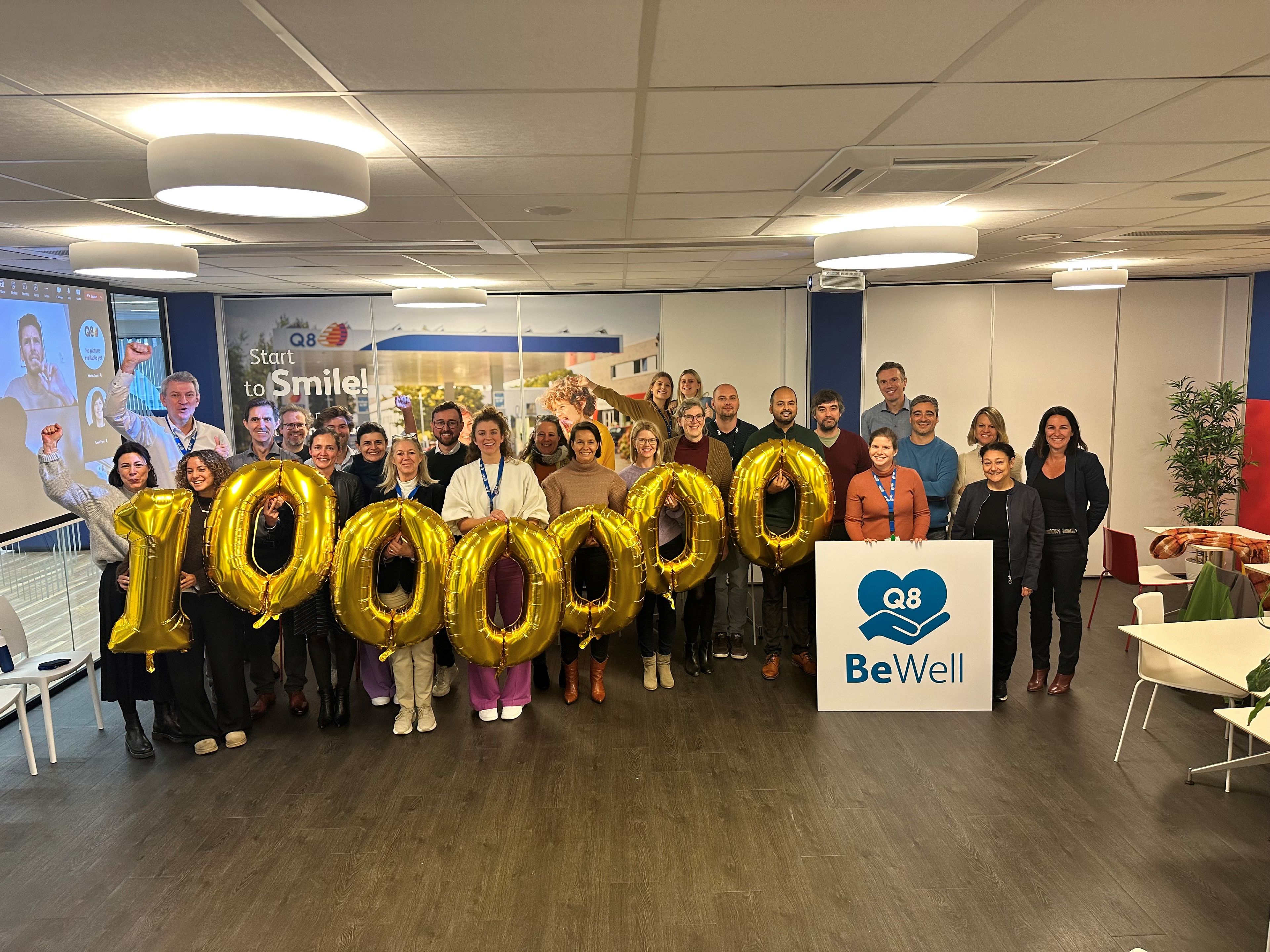 Een grote groep collega's houdt genummerde balonnen vast en er staat een BeWell plakkaat voor hen.