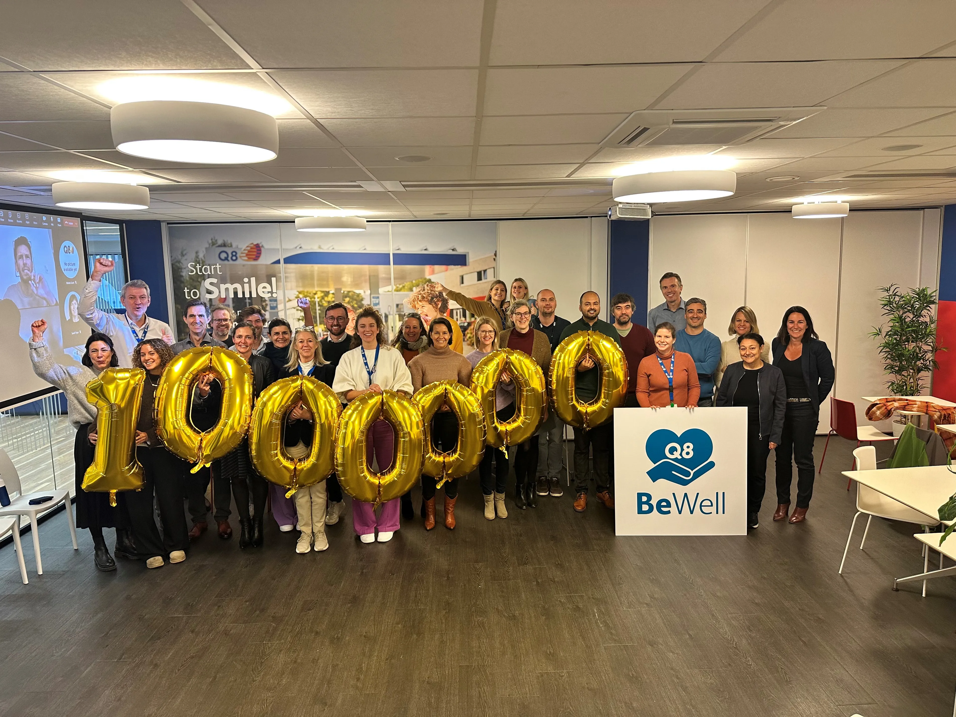 Een grote groep collega's houdt genummerde balonnen vast en er staat een BeWell plakkaat voor hen.