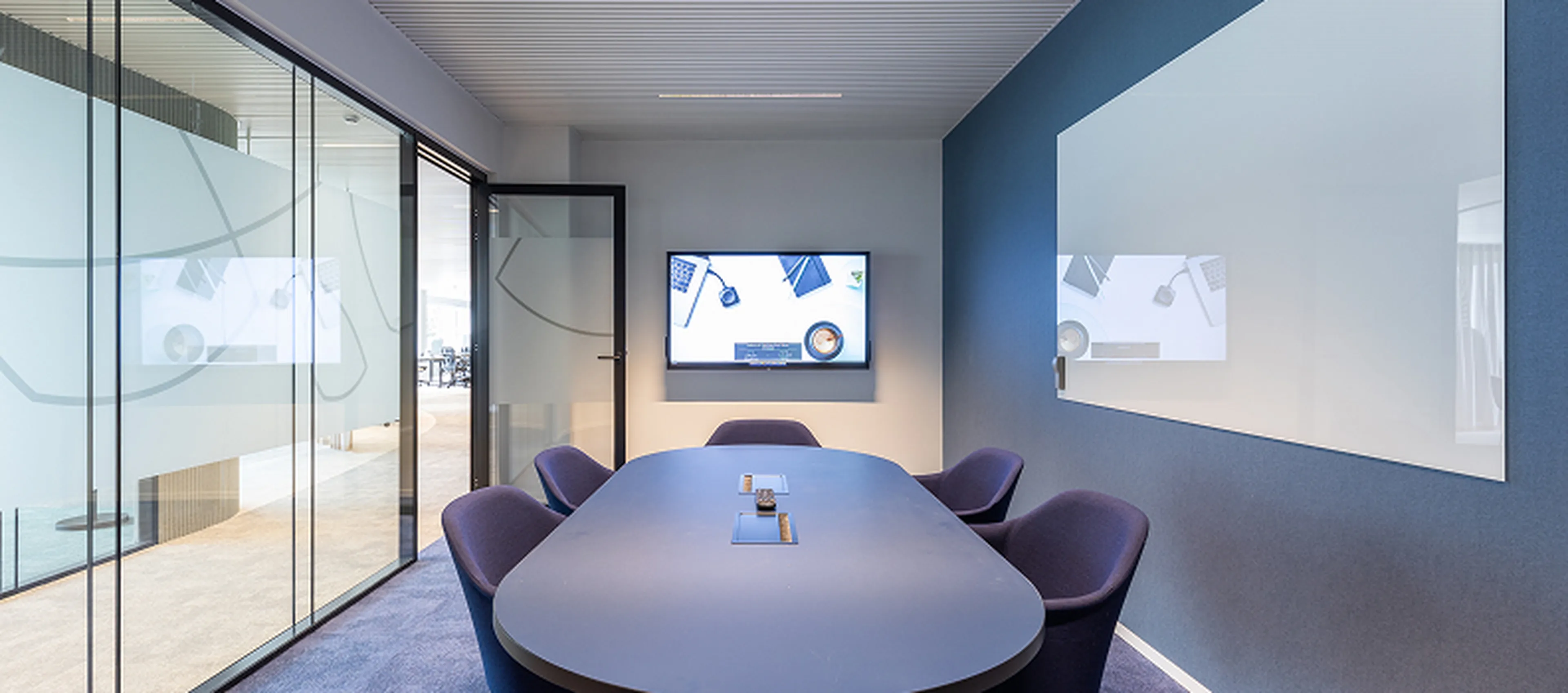 Moderne vergaderruimte in het hoofdkantoor van Q8 in Antwerpen. Glazen wanden, ovale tafel, paarse stoelen en groot whiteboard.