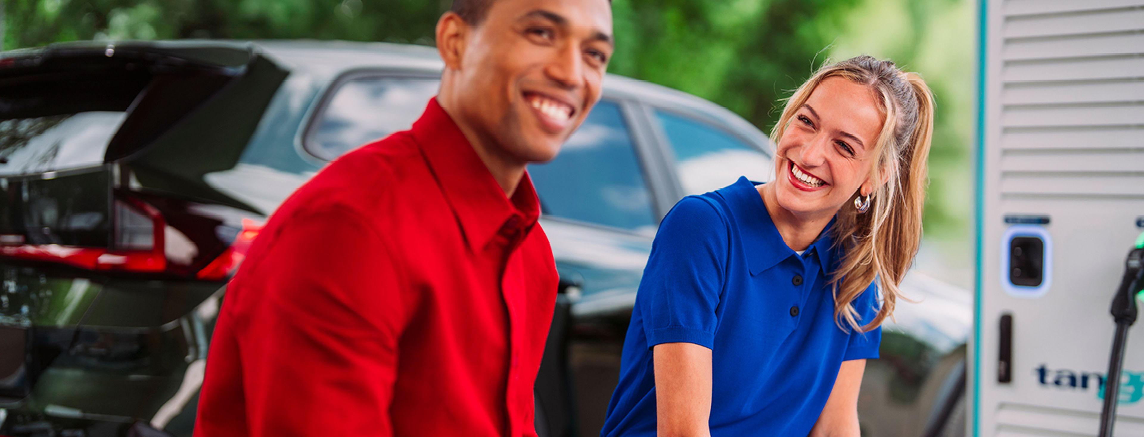 Jonge man en vrouw zitten en glimlachen op een bank tijden het laden van hun auto bij Tango electric