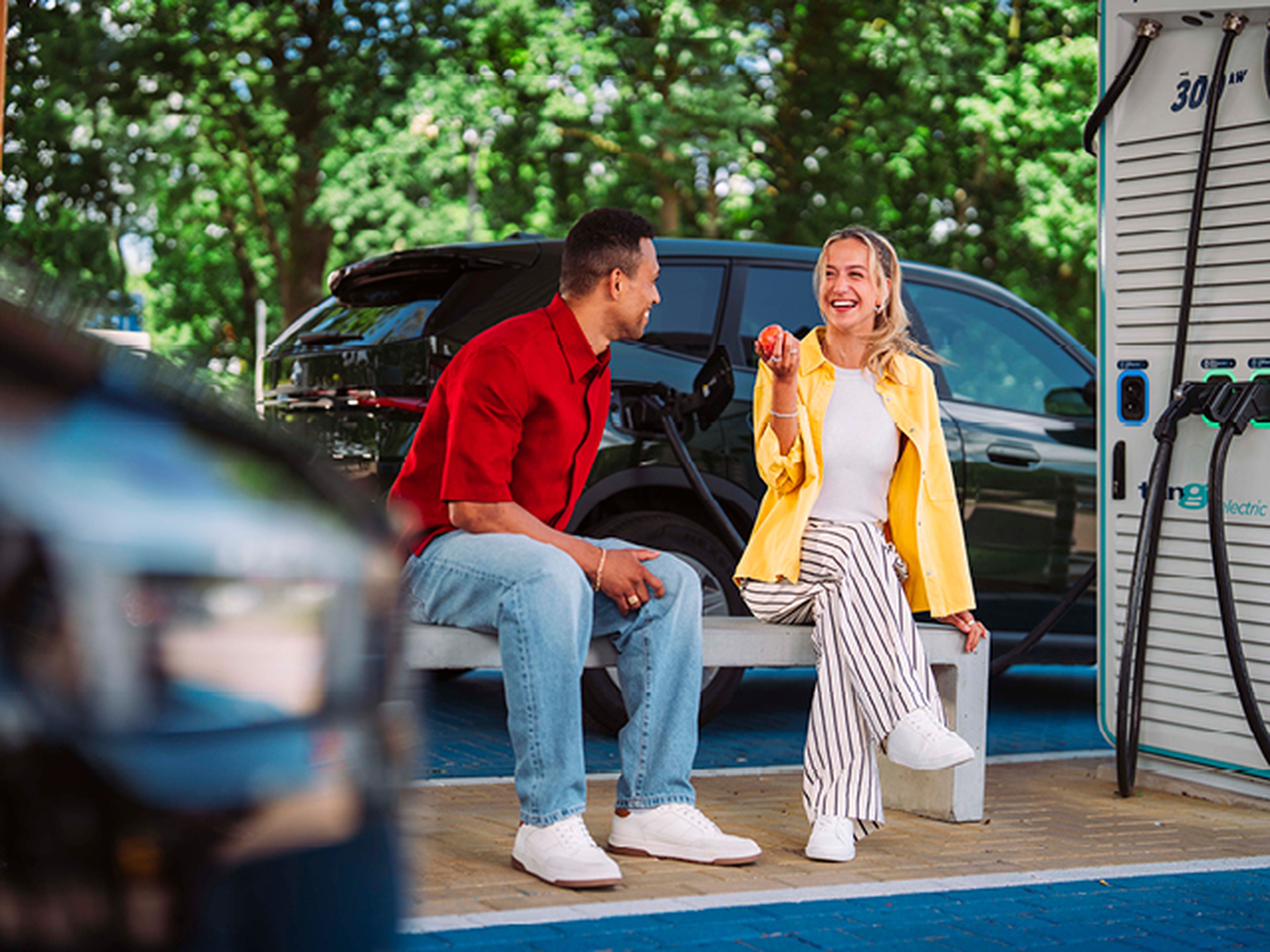 Jonge man en vrouw zitten en glimlachen op een bank tijden het laden van hun auto bij Tango electric