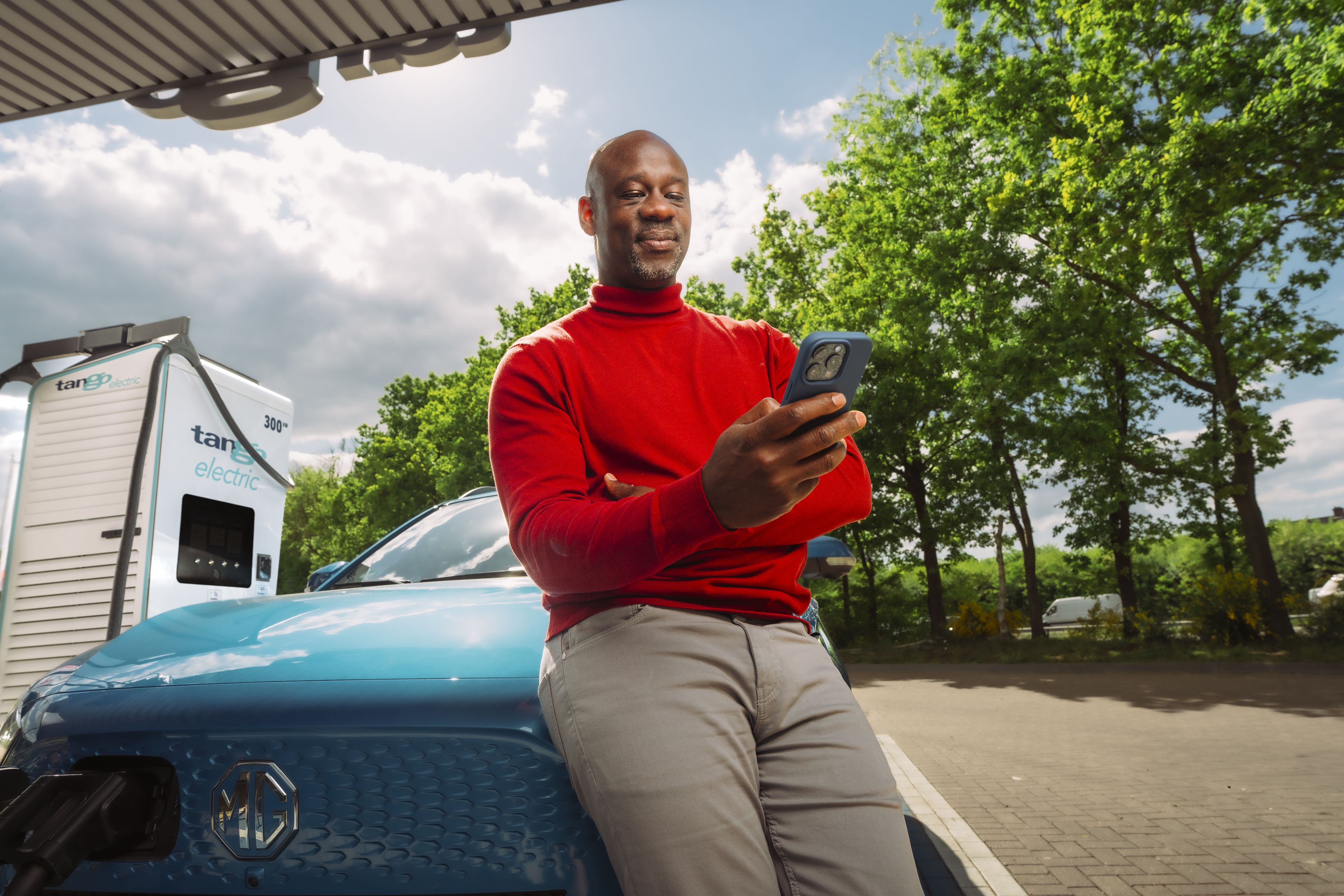 Man leunt tegen auto aan en bekijkt de Tango electric app