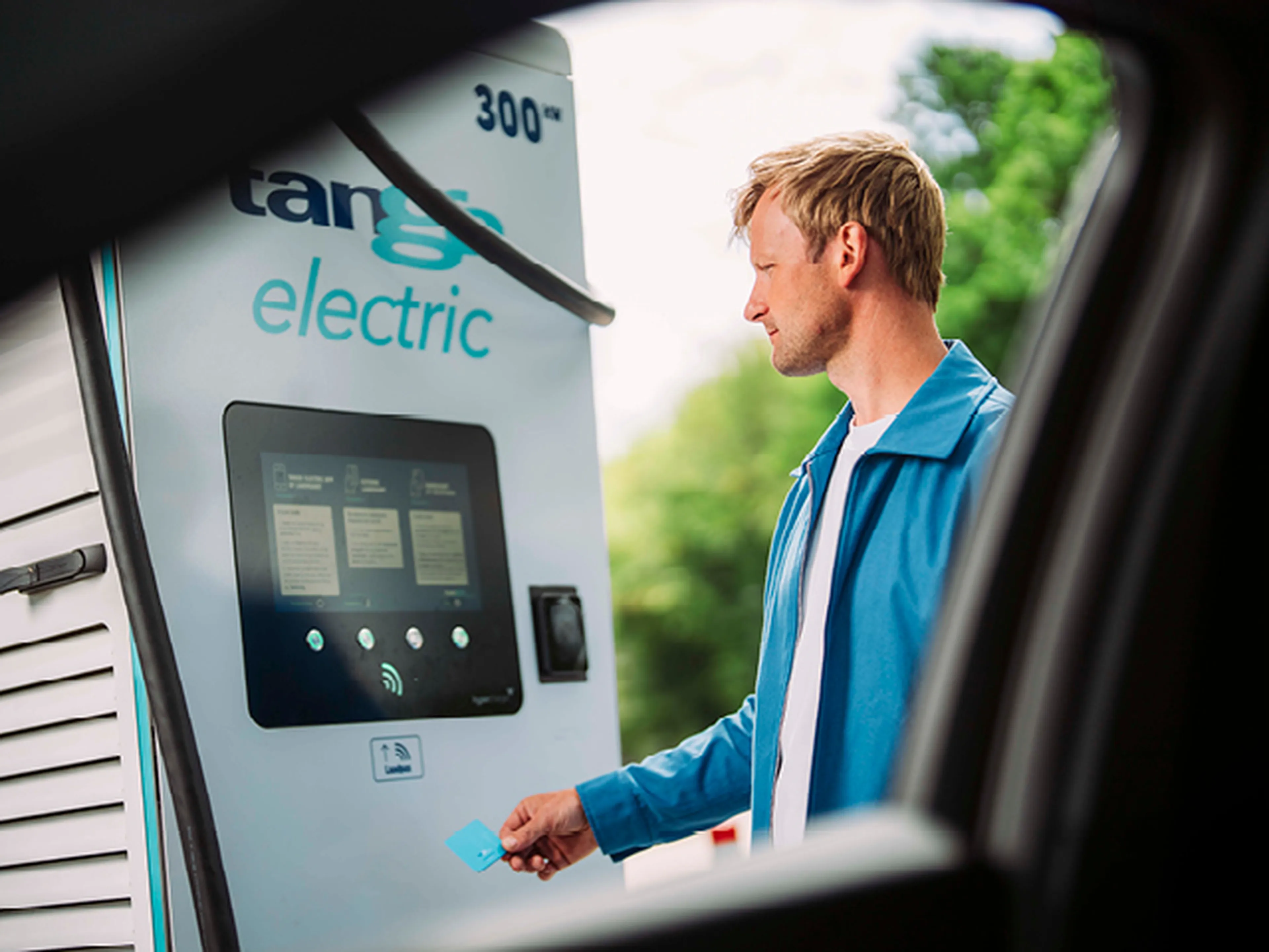 Een persoon in een gele trui houdt een EV-laadstekker naar de camera bij een Q8 electric-laadstation.