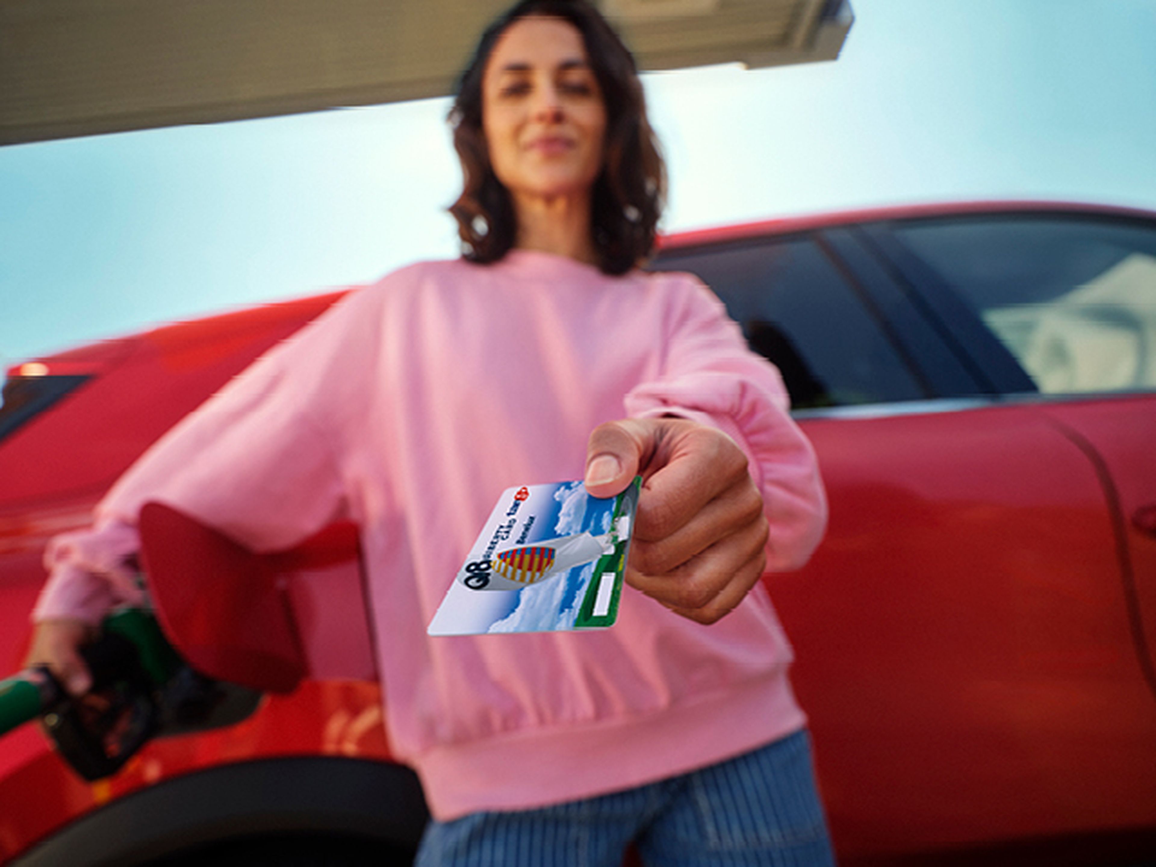 Vrouw toont een Tango Liberty kaart bij haar rode auto aan een Tango station.