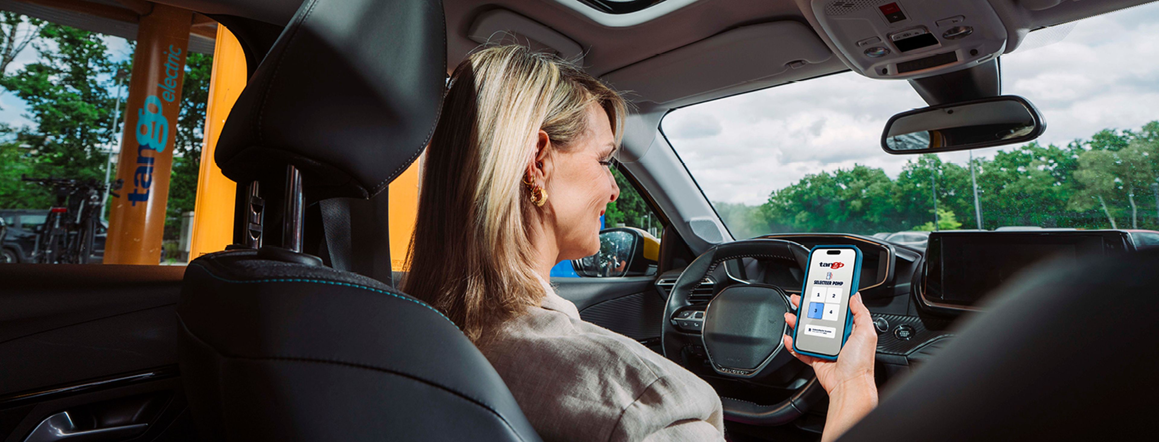 Vrouw zit in auto en gebruikt de Tango app op het tankstation