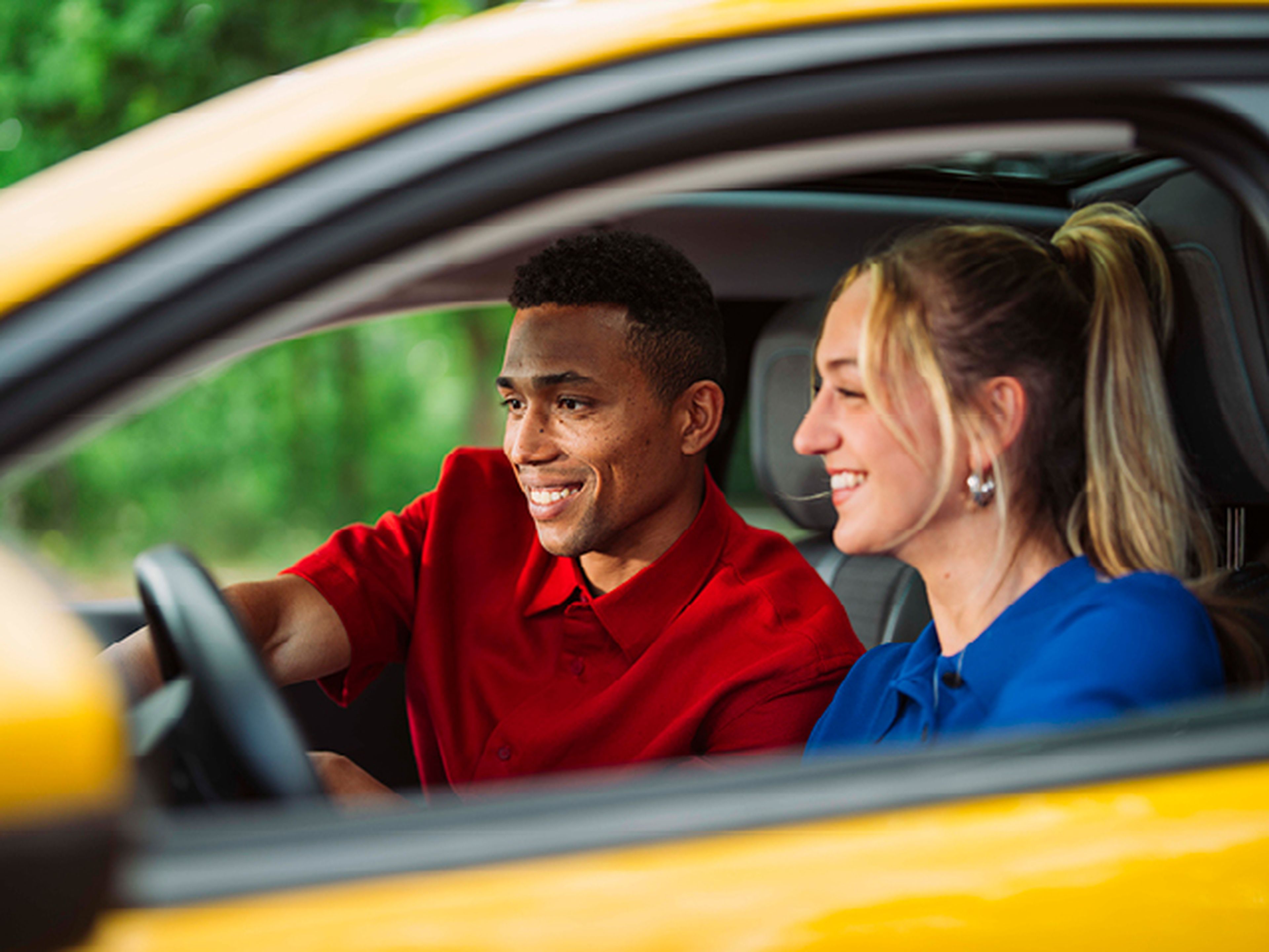 Twee jongeren glimlachen in hun gele peugeot 208