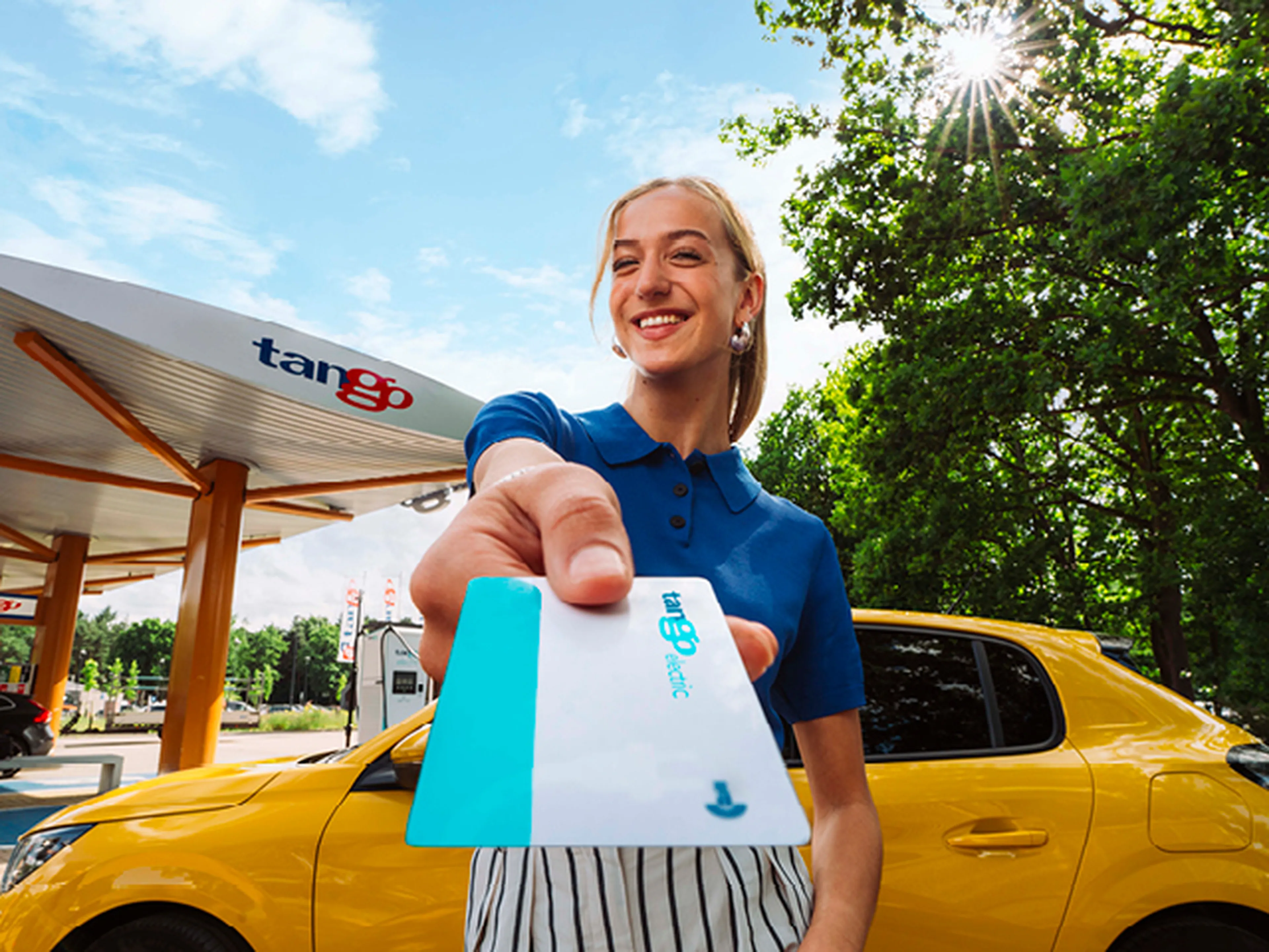 Vrouw die een Tango electric laadpas laat zien bij haar gele elektrische auto en Tango laadstation