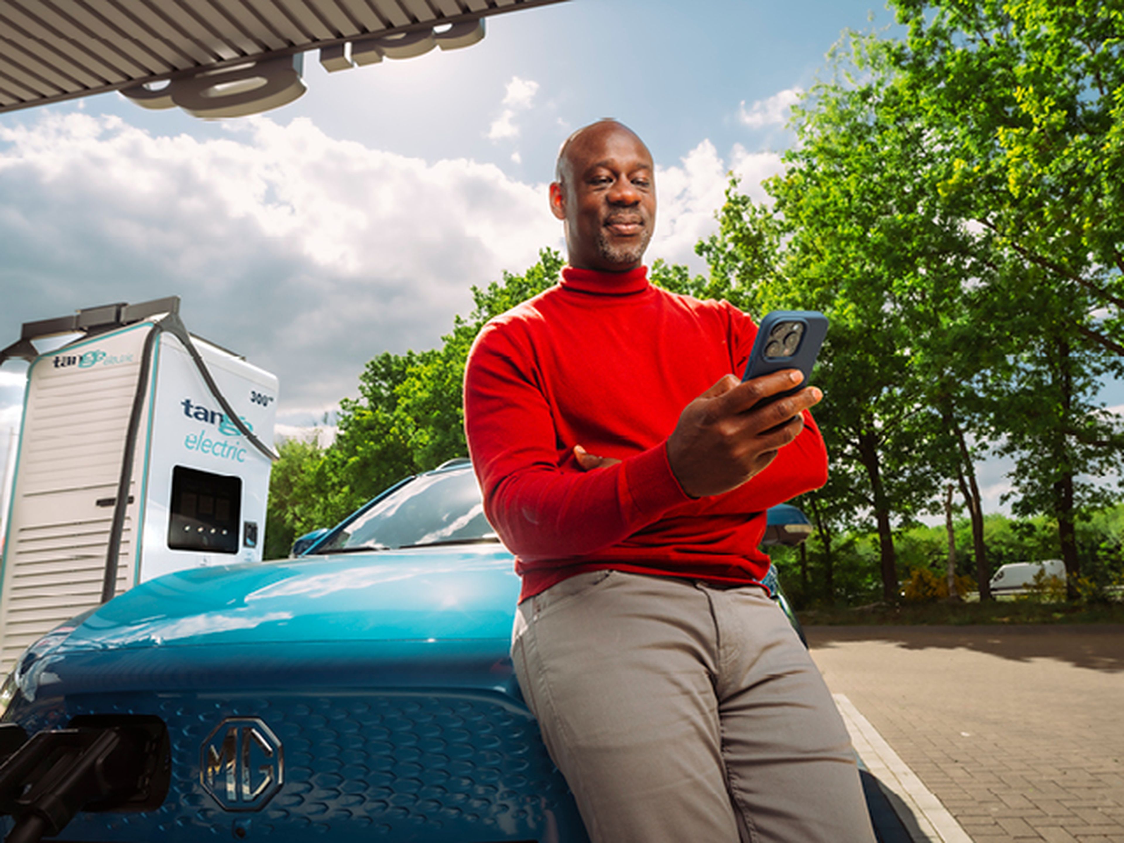 Man leunt tegen blauwe MG tijdens het laden van zijn auto bij Tango electric