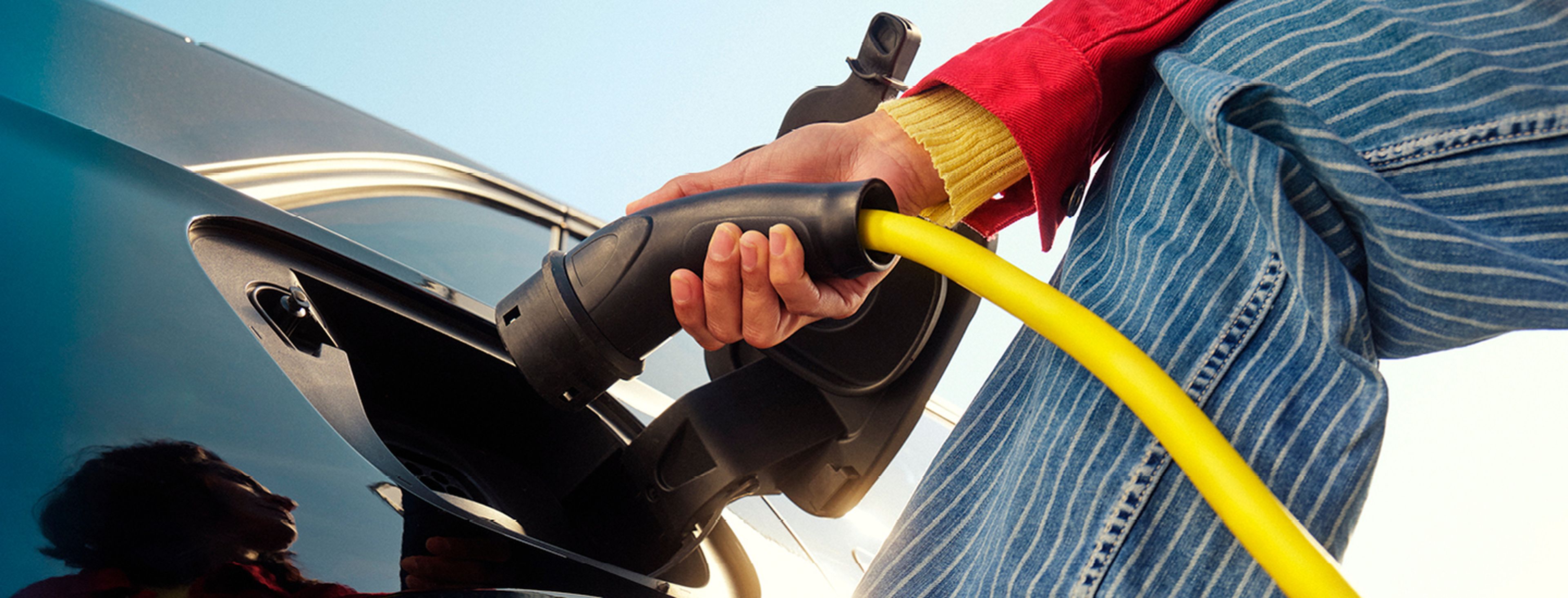 Close-up van een persoon die een gele laadkabel aansluit op een elektrische auto.