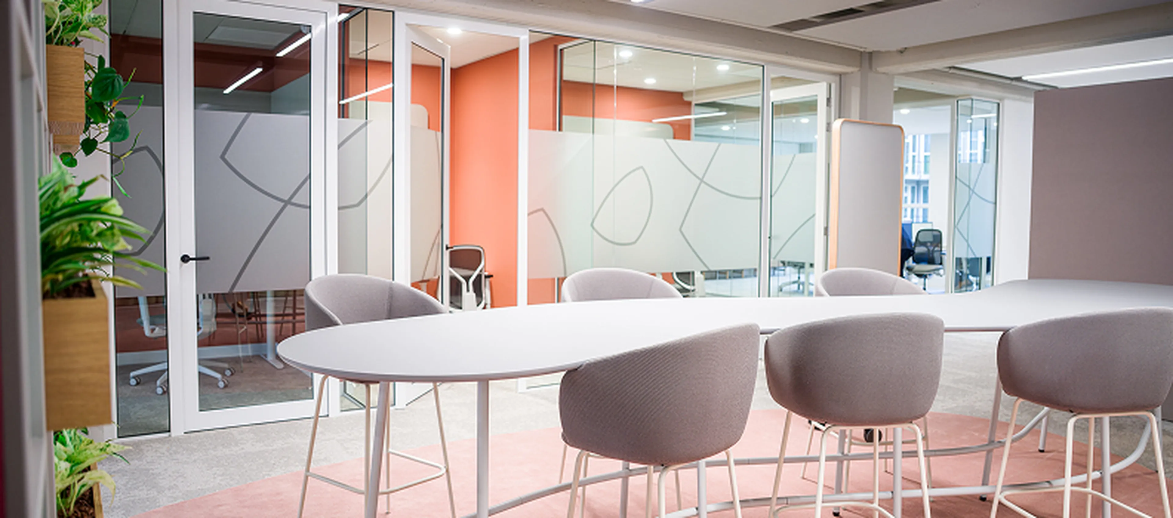 Vergaderruimte in het Q8-hoofdkantoor in Rotterdam met ronde tafels, hoge stoelen en veel glas. Warme kleuren en planten zorgen voor een open en frisse sfeer.