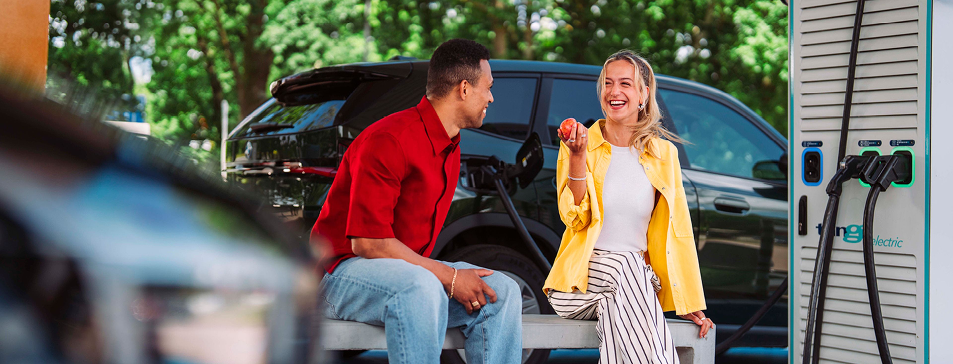 Jonge man en vrouw zitten en glimlachen op een bank tijden het laden van hun auto bij Tango electric