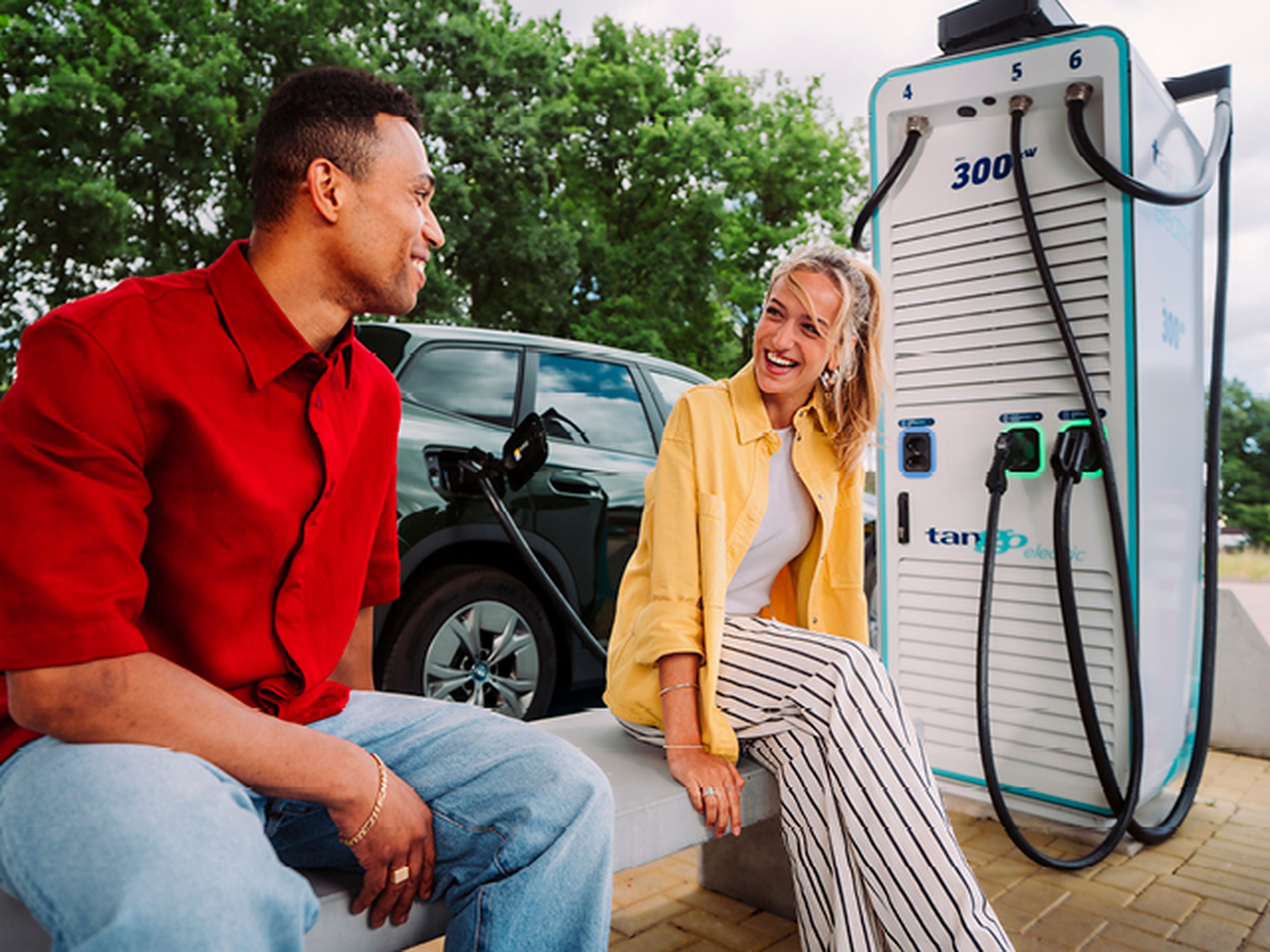 Jonge man en vrouw zitten en glimlachen op een bank tijden het laden van hun auto bij Tango electric
