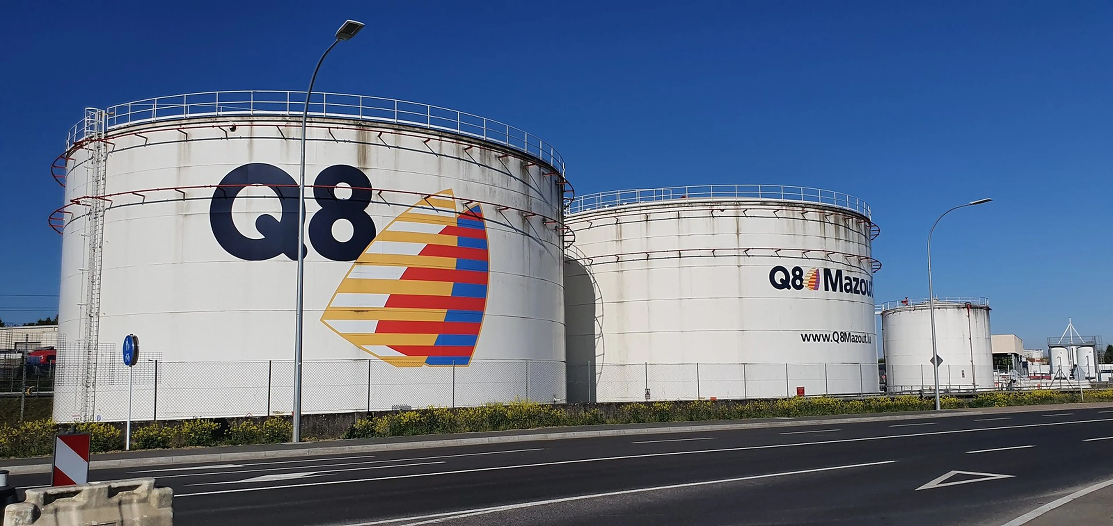 Drie grote witte opslagtanks van Q8 langs een weg, met het Q8-logo op de linkertank.