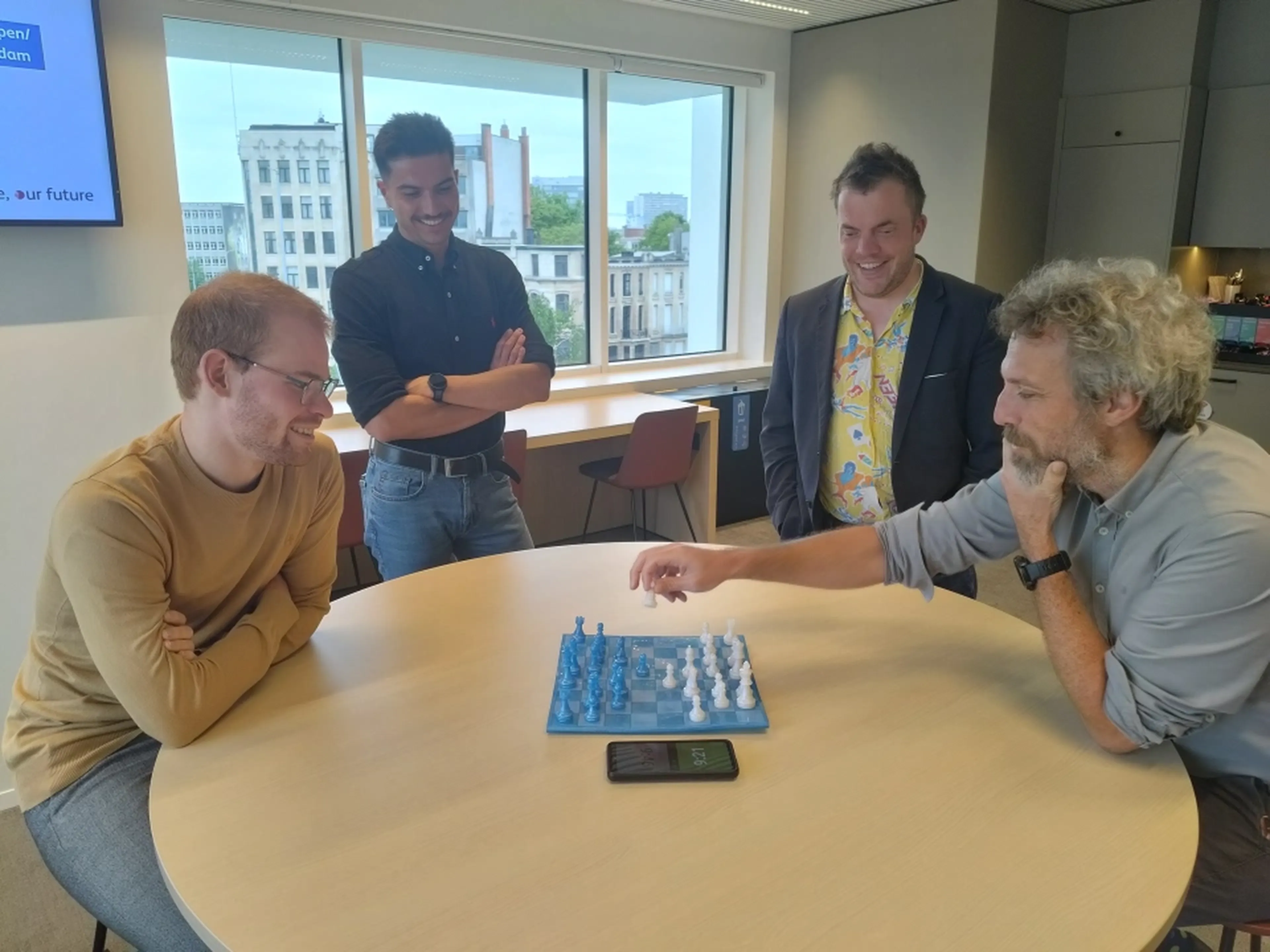 Twee Q8 collega's spelen een schaakspel tegen elkaar terwijl twee andere collega's kijken.