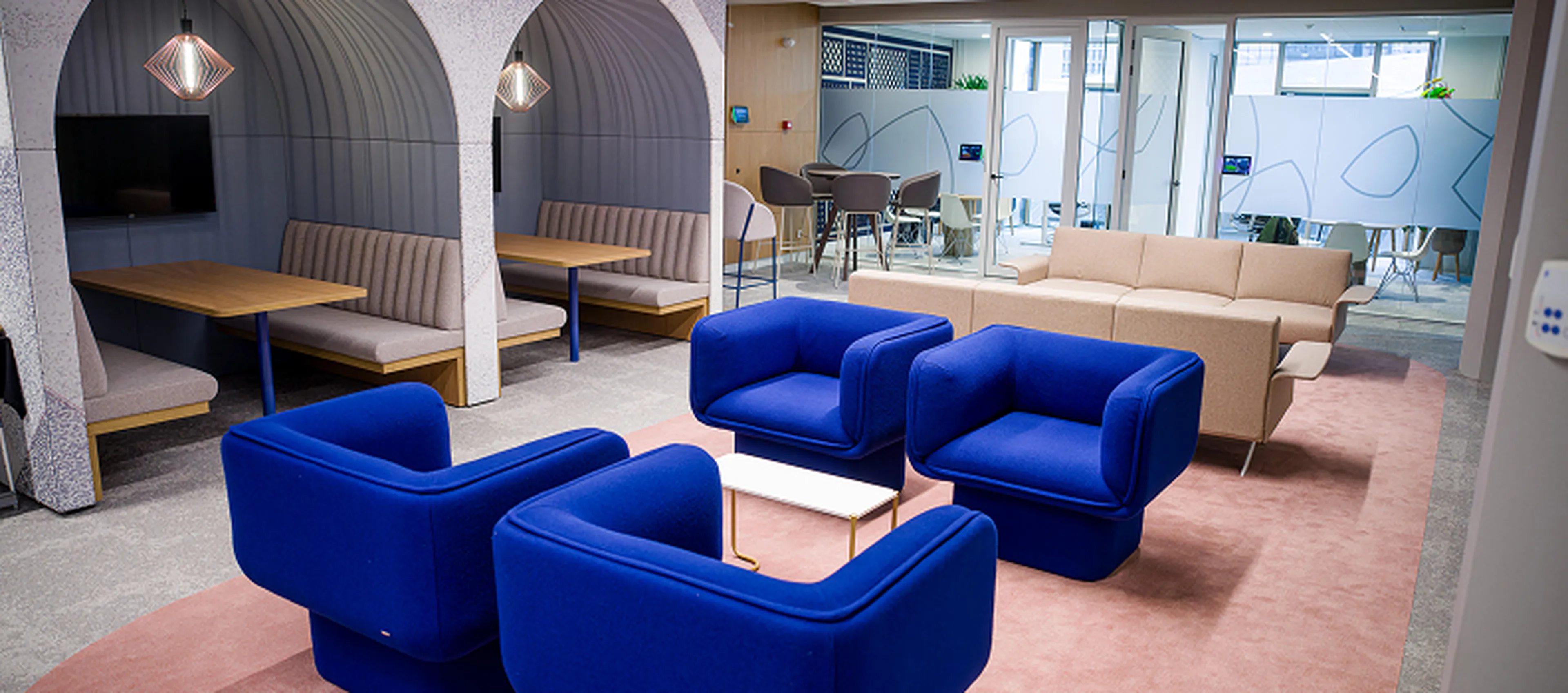 Loungehoek in het Q8-hoofdkantoor in Rotterdam met felblauwe zetels, beige sofa’s en overdekte zitnissen met tafels.