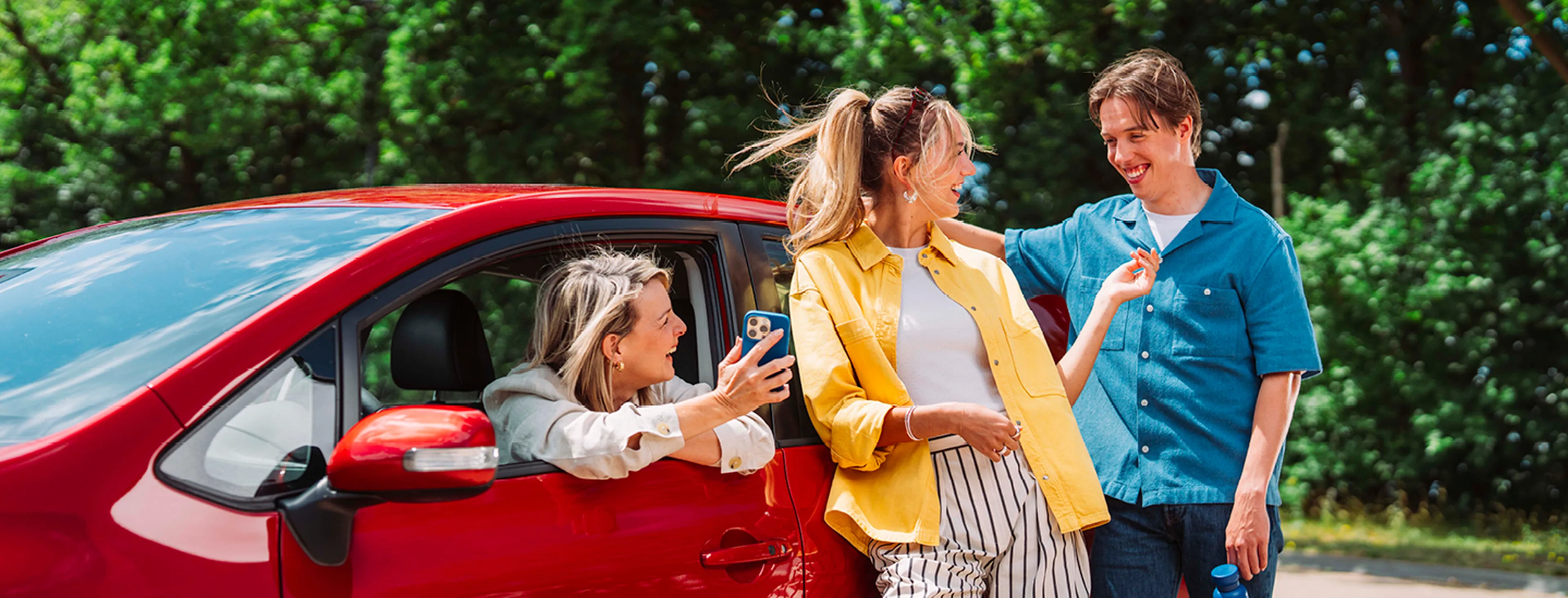 Vrouw zit in de auto en toont haar smartphone aan haar vrienden die tegen de auto leunen